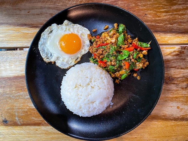 Arroz coberto com carne de porco frita e manjericão com um ovo frito na mesa