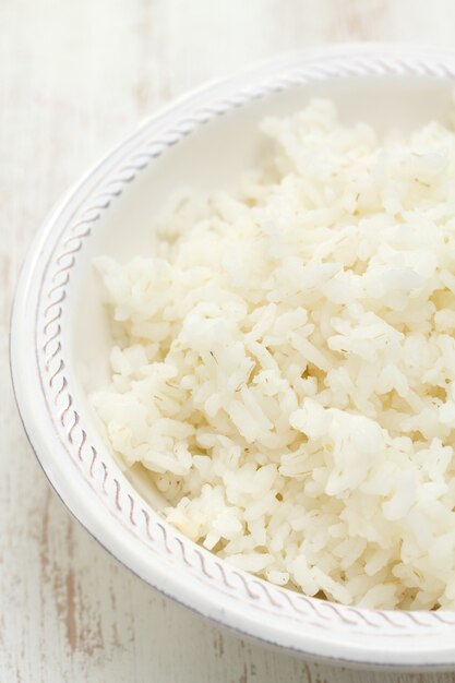 Arroz cozido na tigela branca em branco de madeira