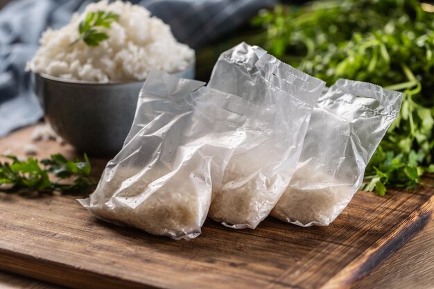 Arroz crudo en bolsas de plástico sobre fondo de madera y arroz cocido en tazón