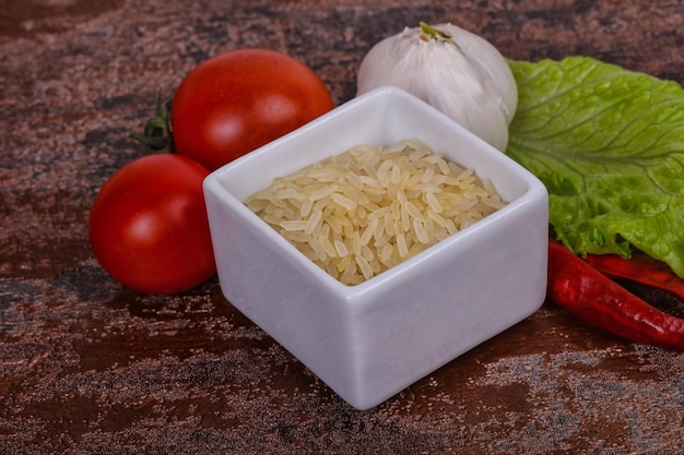 Arroz crudo crudo en el tazón servido con pimienta y hojas de ensalada