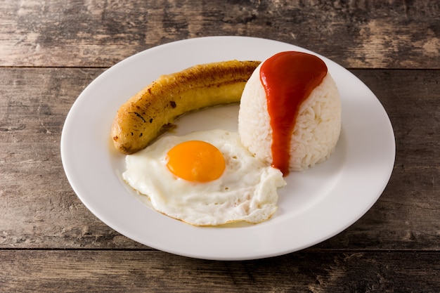 Arroz a la cubana Arroz típico cubano con plátano frito y huevo frito en un plato sobre la mesa de madera