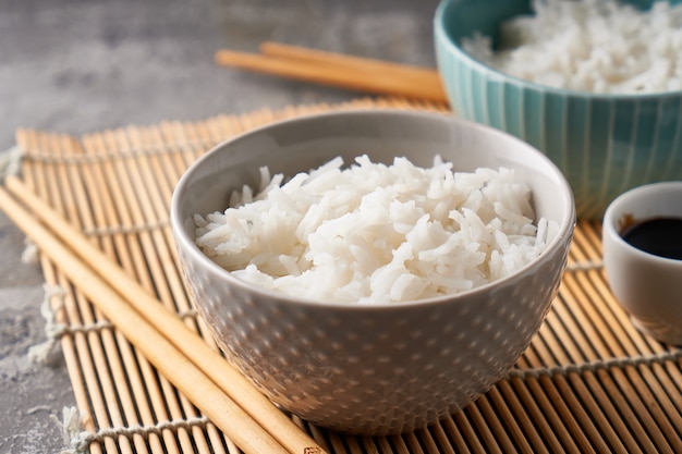 Arroz en un cuenco de porcelana, con palillos japoneses, salsa de soja, servido en una mesa de piedra gris Espacio de copia