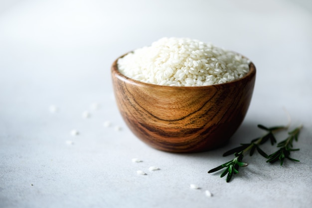 arroz de jasmim orgânico cru em tigela de madeira e alecrim em concreto claro. Ingredientes alimentares. Espaço da cópia