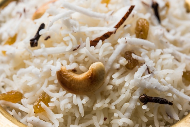 Arroz dulce de coco O Narali Bhat en marathi, adornado con anacardos, clavo y frutos secos, servido en un cuenco de latón sobre un fondo de mal humor. Enfoque selectivo