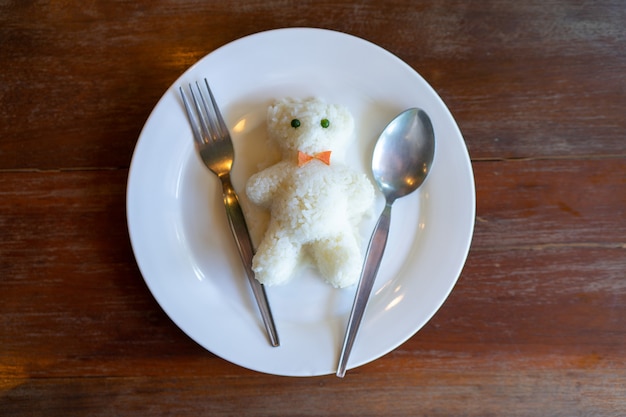 Arroz em prato branco docurado como boneco de urso na mesa de madeira