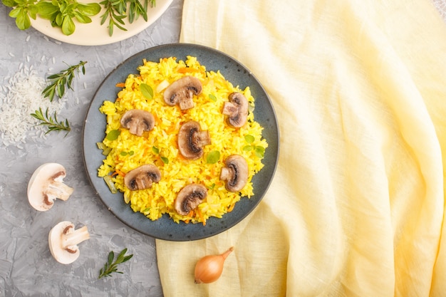 Arroz frito amarillo con champiñones champiñones cúrcuma y orégano en placa de cerámica azul sobre un fondo de hormigón gris