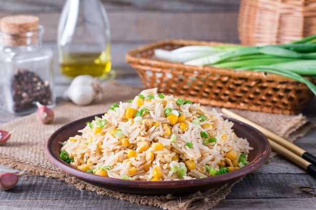 Arroz frito asiático con huevos y maíz en el plato sobre fondo de madera