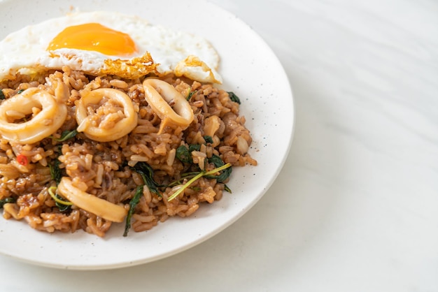 Arroz frito con calamares y huevo frito cubierto de albahaca al estilo tailandés