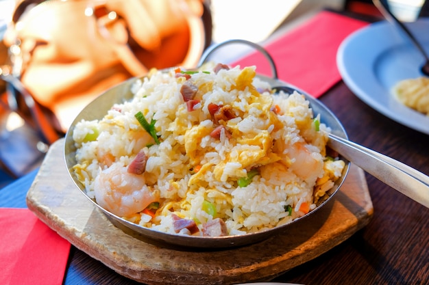 Arroz frito con el camarón en una cacerola caliente usada como placa con la tabla de madera en fondo.