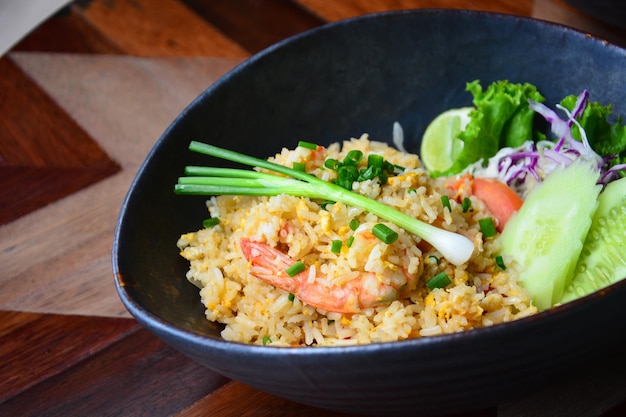 Foto arroz frito com camarão e ovo em tigela de cerâmica no fundo da mesa de madeira