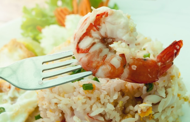 Arroz frito com camarão e ovo frito no prato branco na mesa de madeira