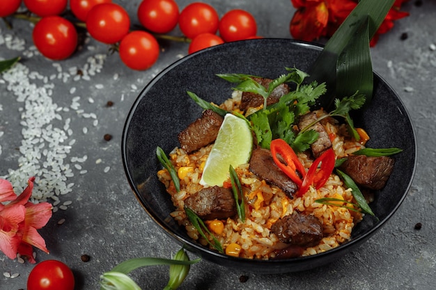 Arroz frito com carne e legumes em uma mesa cinza.