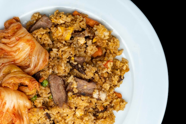 Arroz frito con cordero asado en rodajas y kimchi en un plato blanco aislado en topview negro o flatlay