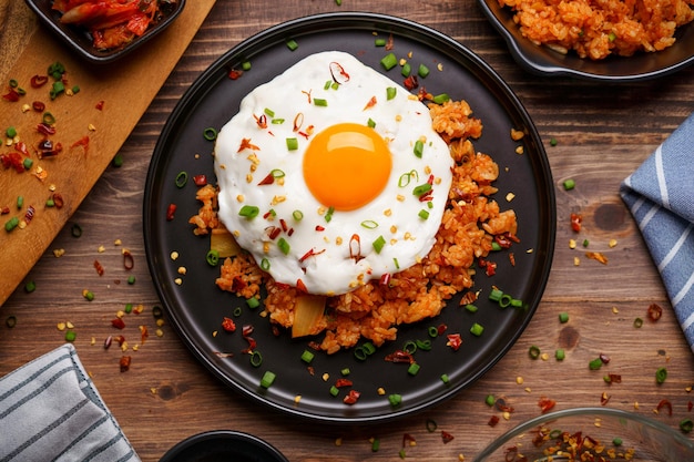 Arroz frito con kimchi cubierto con huevo frito y repollo kimchi fresco en un recipiente sobre fondo de madera colocado. Estilo de comida coreana