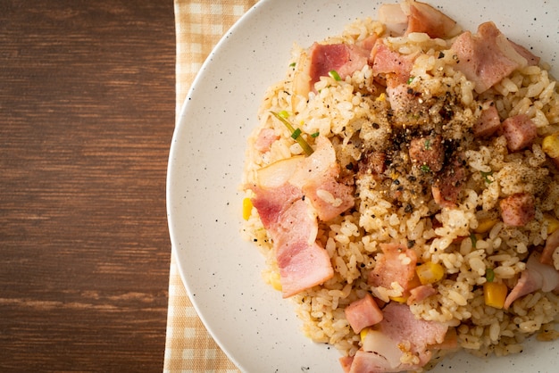 Arroz frito con tocino, jamón y pimientos negros en la placa blanca.