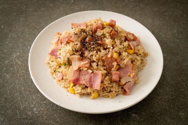 Arroz frito con tocino, jamón y pimientos negros en la placa blanca.