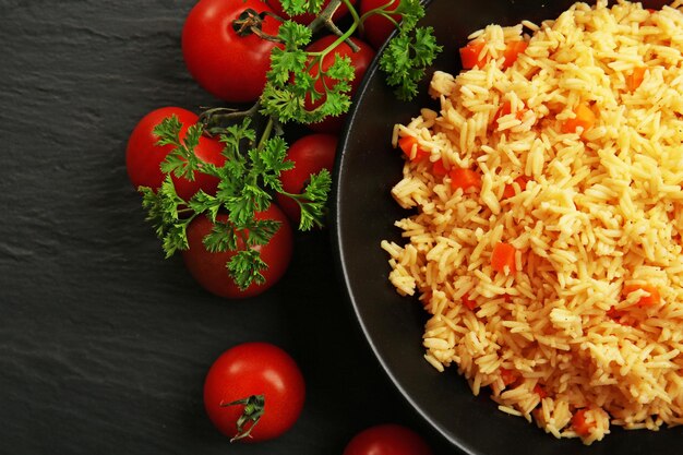 Arroz guisado con zanahoria y tomates en un plato sobre fondo negro de cerca