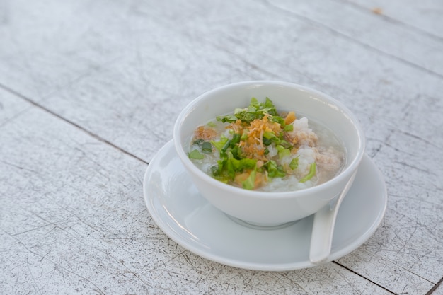 Arroz hervido con carne de cerdo en un tazón blanco sobre fondo blanco de mesa de madera