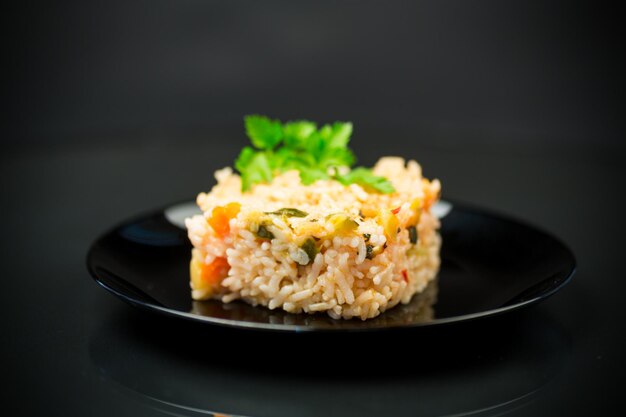 Arroz hervido cocido con zanahorias calabacín y verduras en un plato aislado sobre fondo negro