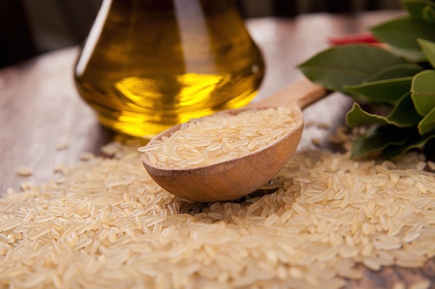 Foto arroz integral crudo con cuchara de aceite de oliva y fondo leñoso