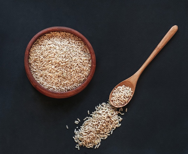 Arroz integral em uma tigela de madeira com uma colher de pau em fundo preto, vista superior