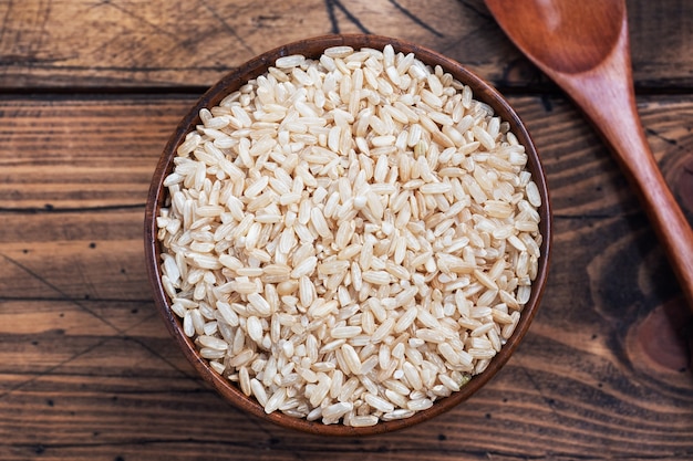 Arroz integral de grano largo crudo en un recipiente, espacio de copia de mesa de madera, vista superior.