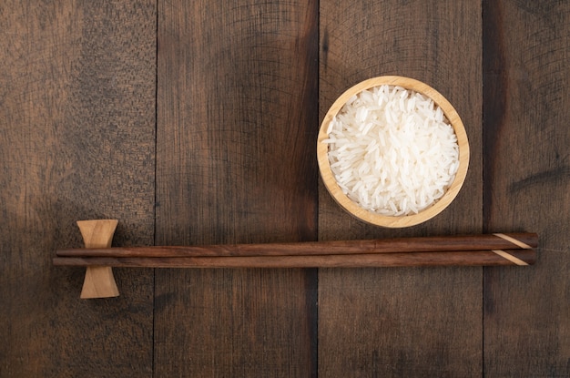 Arroz jazmín en un tazón de madera y palillos en el fondo de la tabla de madera de grunge con espacio de copia, vista superior