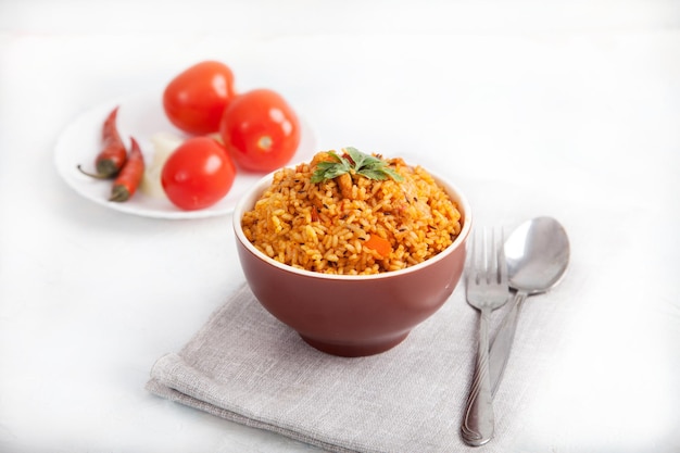 Arroz Jollof com salsa em uma xícara de cerâmica tomate e pimentão em um guardanapo de linho em um fundo branco Cozinha nacional da África