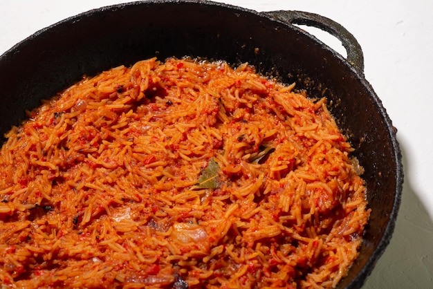 Arroz jollof en una sartén sobre un fondo blanco Un plato tradicional nigeriano de tomates de arroz y especias