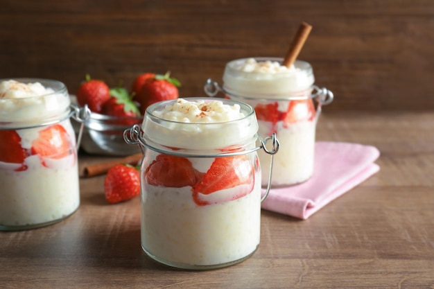 Arroz con leche cremoso con fresa en tarros sobre mesa de madera