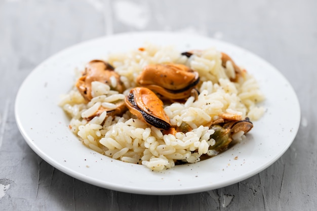 Arroz con mejillones en un pequeño plato blanco sobre fondo de cerámica