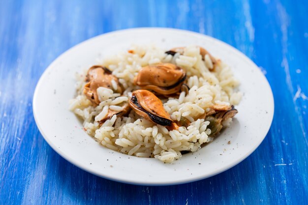 Arroz con mejillones en un pequeño plato blanco sobre fondo de madera azul