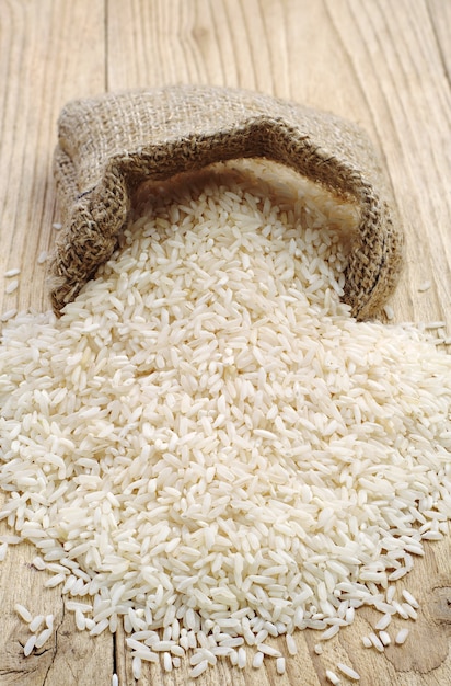 Arroz en mesa de madera y pequeño saco de arpillera