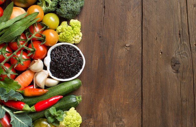 Arroz negro crudo en un recipiente con verduras sobre madera