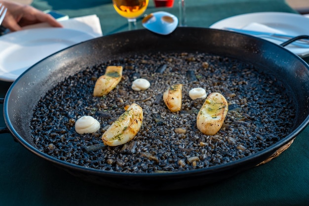 Arroz negro con sepia y ajos tiernos un plato de arroz seco cocinado en paella o en cazuela de barro un sabor característico de la cocina mediterránea valenciana España