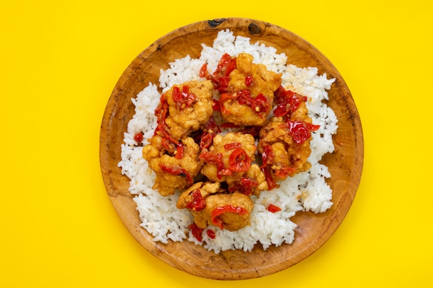 El arroz con nuggets de pollo espolvoreado con salsa de chile se sirve en un plato de madera.