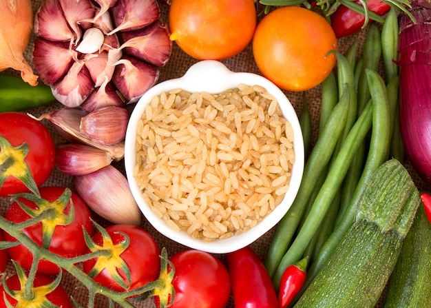 Foto arroz orgânico inteiro inteiro na tigela entre vista superior de vegetais crus