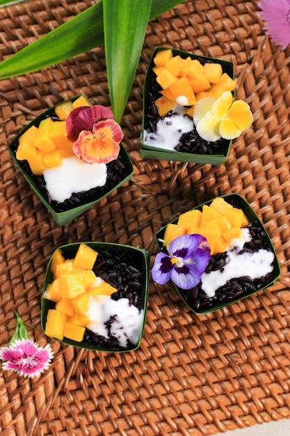 Arroz pegajoso caseiro de coco preto com manga em copo de folhas pandan, foco seletivo com cobertura de flores comestíveis de amores-perfeitos