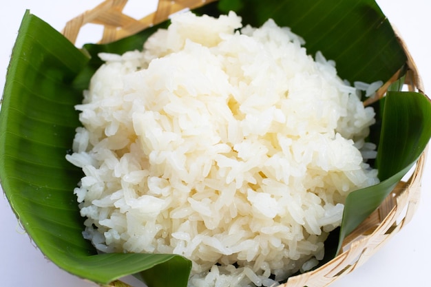 Arroz pegajoso en hoja de plátano en cesta de bambú sobre fondo blanco.