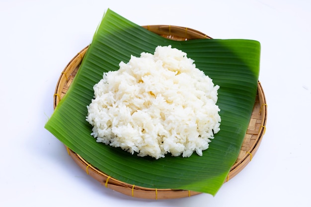 Arroz pegajoso en hoja de plátano en cesta de bambú sobre fondo blanco.