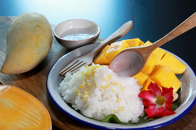 Arroz pegajoso del mango con la cuchara de madera que vierte leche de coco en la placa blanca.