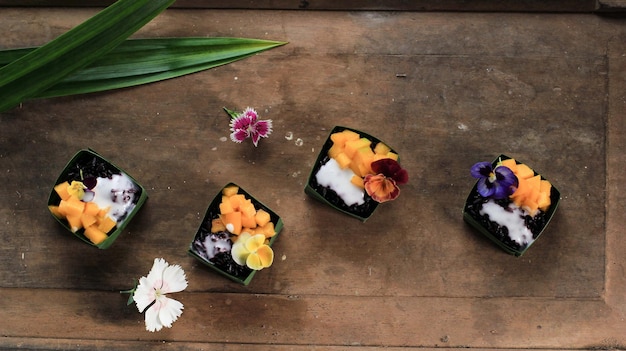 Arroz pegajoso negro de coco casero con mango en taza de hojas de pandan, enfoque selectivo con cobertura de flores de Edibel de pensamientos