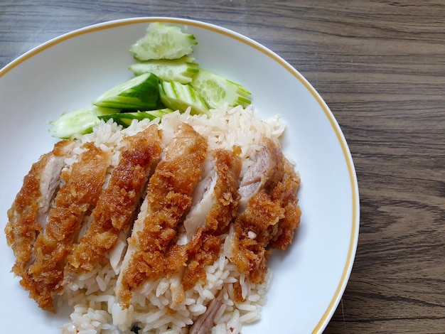 Arroz con pollo de Hainan con rodajas de pepino de pollo frito y sopa de pollo sobre fondo de madera