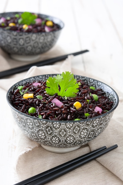 Arroz preto em uma tigela e legumes na mesa de madeira branca