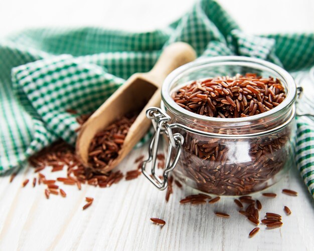 Arroz rojo crudo en frasco de vidrio sobre una superficie de madera blanca