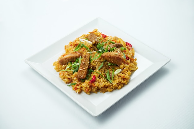 Arroz saboroso wok em molho agridoce com legumes e carne de porco em um prato branco sobre uma mesa cinza. Feche acima do iew. Cozinha asiática