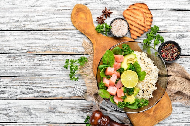 Arroz con salmón, aguacate y espinacas En un plato negro sobre un fondo de madera Vista superior Espacio libre para su texto Plano