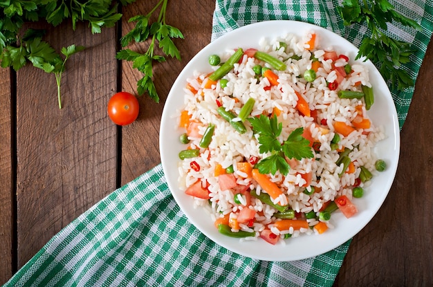 Arroz saudável apetitoso com legumes em chapa branca sobre uma mesa de madeira