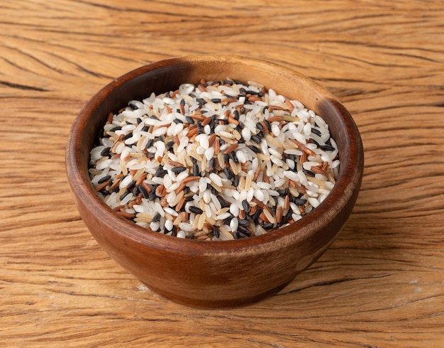 Arroz sortido cru em uma tigela sobre a mesa de madeira.