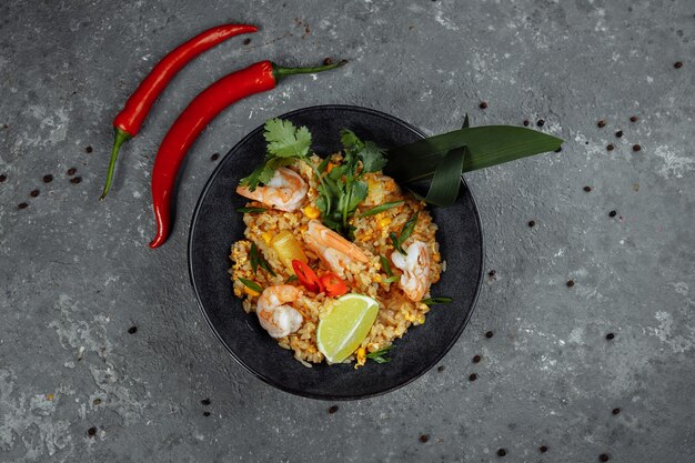 Arroz tailandês com camarão em uma placa preta no escuro.